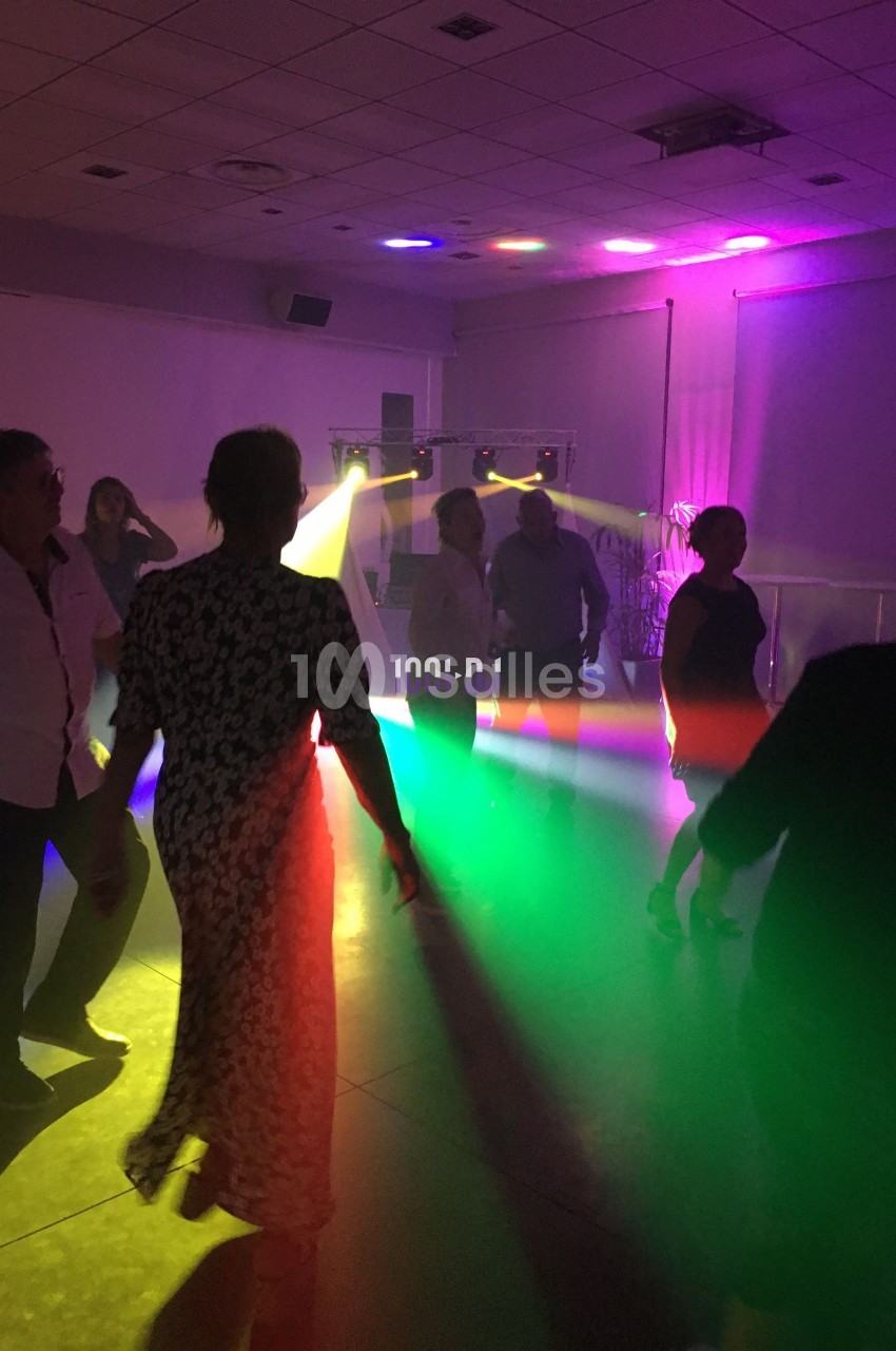 Des personnes dansent dans une salle sombre éclairée par des lumières colorées et des projecteurs.