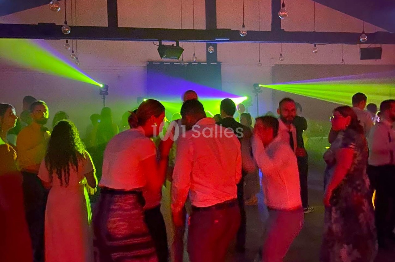 Des personnes dansent dans une salle sombre éclairée par des lumières colorées et des faisceaux lumineux.