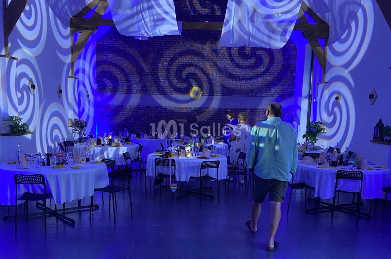 Salle de réception décorée avec des tables rondes dressées, éclairage bleu et motifs lumineux projetés sur les murs.