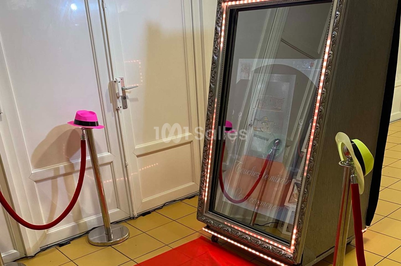 Miroir interactif encadré de lumières, posé sur un tapis rouge avec des chapeaux colorés à proximité.