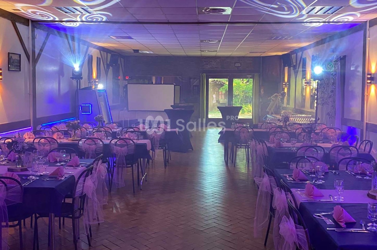 Salle de réception décorée avec des tables dressées, nappes roses et éclairages d'ambiance violets.
