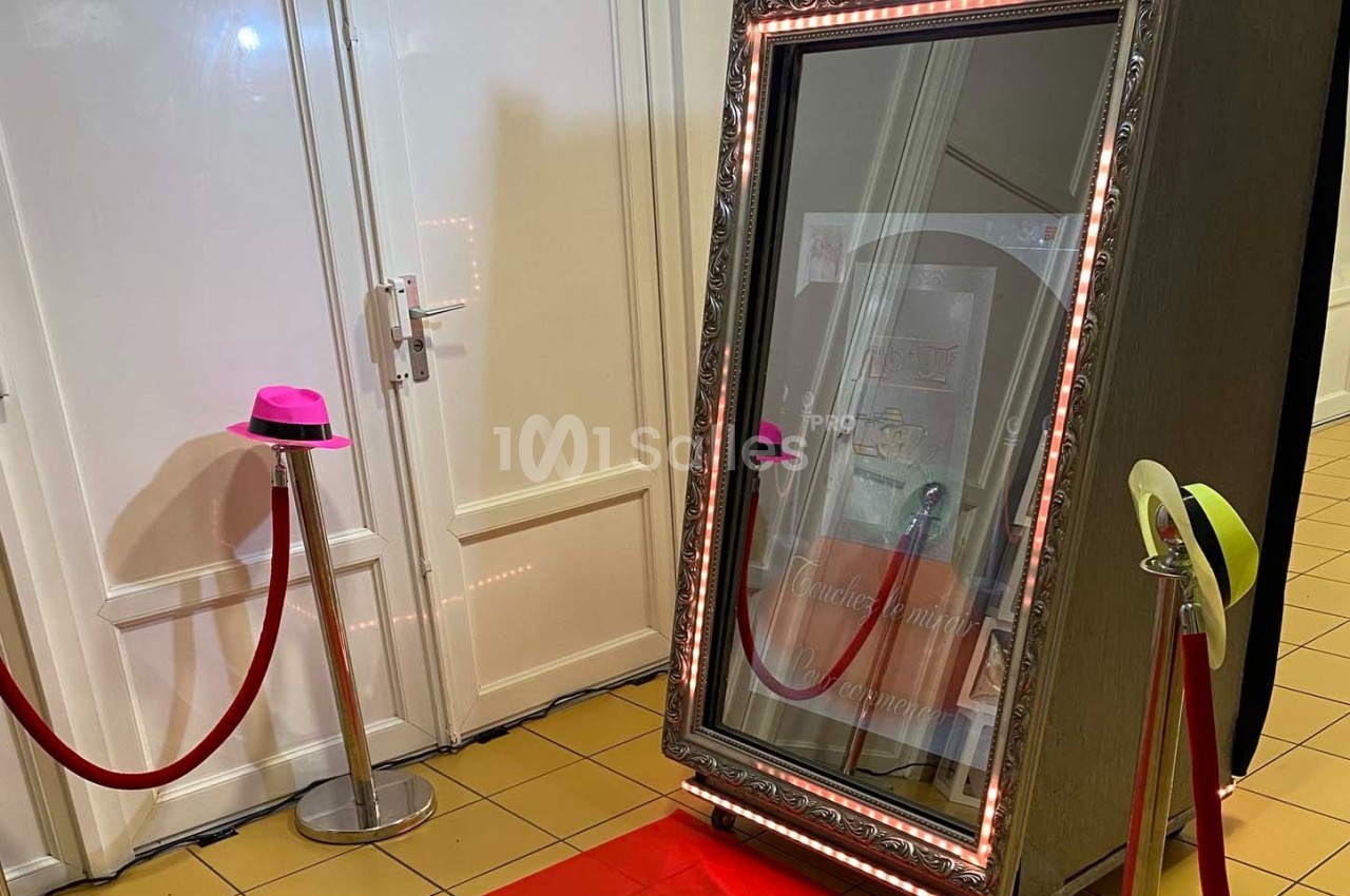 Miroir interactif encadré, entouré de lumières LED, placé sur un tapis rouge avec des accessoires colorés à proximité.