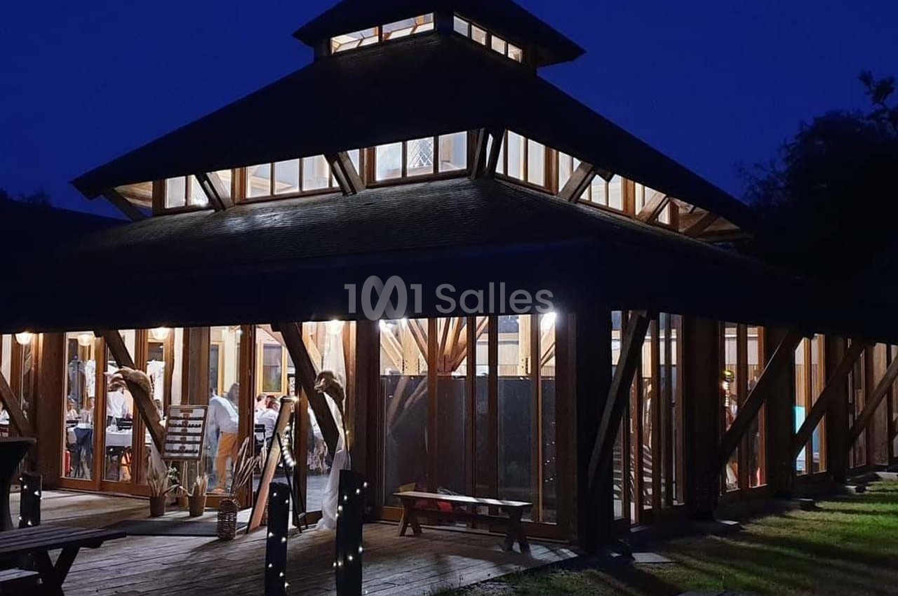 Bâtiment en bois avec de grandes baies vitrées éclairé de l'intérieur, entouré d'herbe et photographié de nuit.