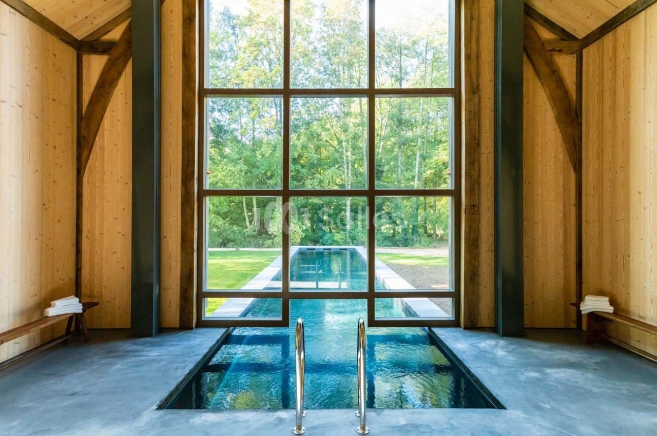 Piscine intérieure avec baies vitrées donnant sur un jardin verdoyant, entourée de murs en bois clair.