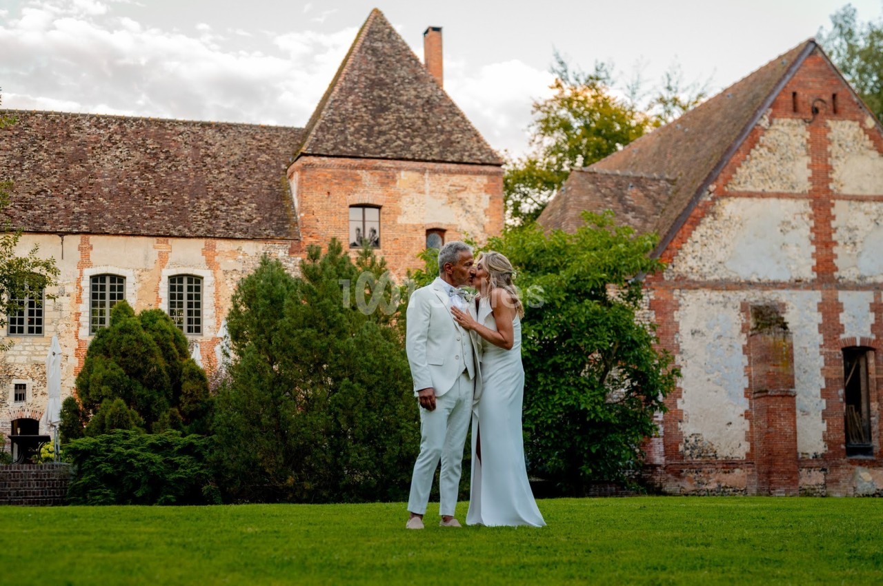 Un couple en tenue élégante se tient tendrement dans un jardin devant un bâtiment ancien en pierre.