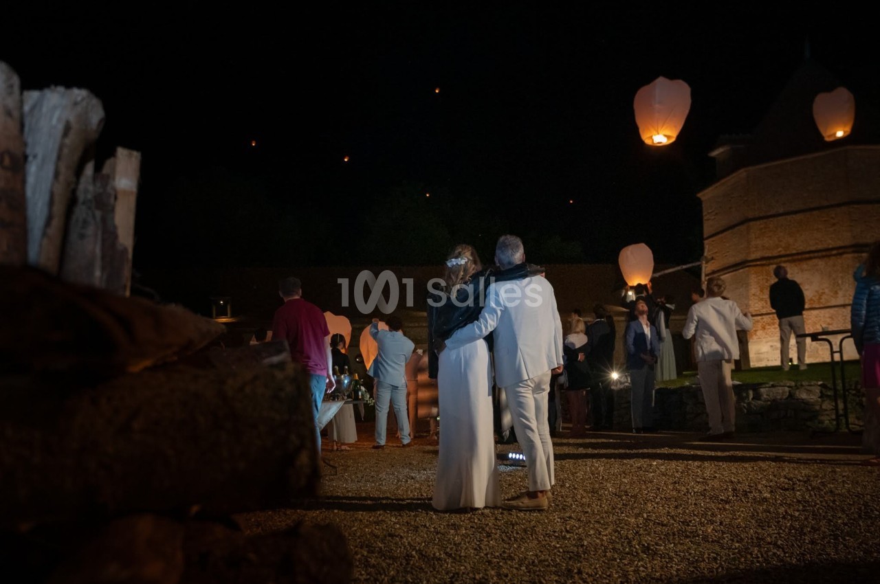 Un couple de dos observe des lanternes volantes dans un cadre nocturne entouré de convives.