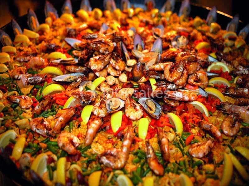 Plat de paella garnie de crevettes, moules, calamars, légumes colorés et quartiers de citron.