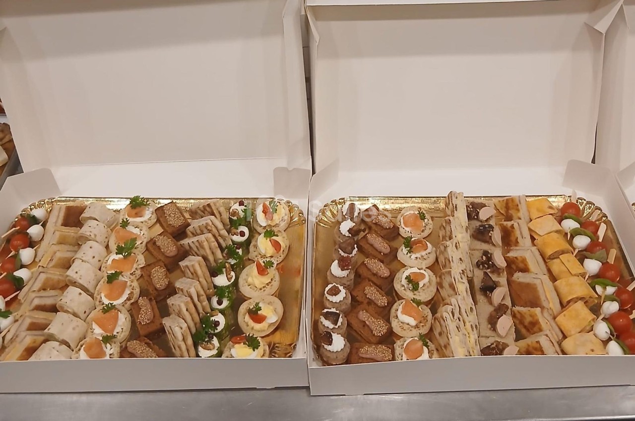Plateaux garnis de divers amuse-bouches, incluant toasts, roulés, œufs mimosa et bouchées salées, présentés dans des boîtes…