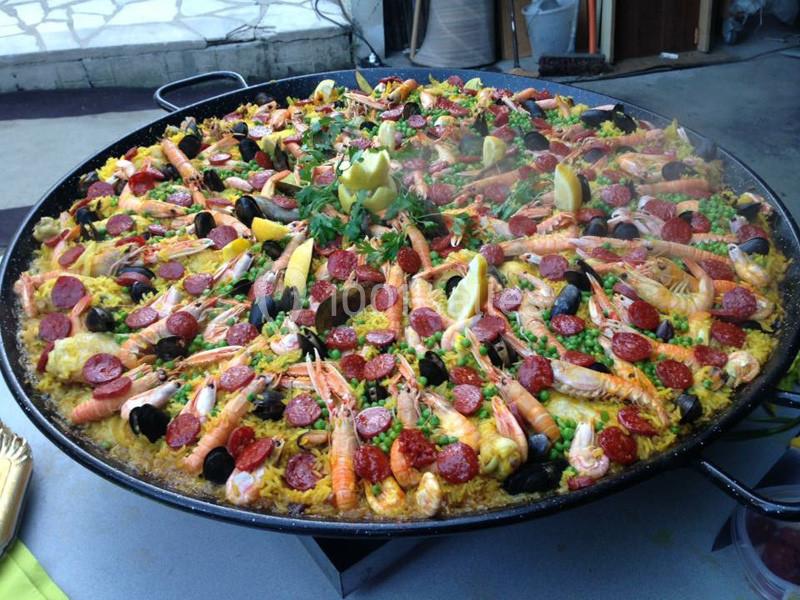 Grande poêle de paella garnie de fruits de mer, chorizo, légumes et quartiers de citron, décorée de persil.