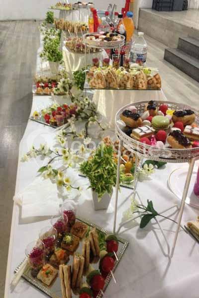 Buffet dressé avec des plateaux de pâtisseries, sandwichs, fruits et boissons, décoré de fleurs blanches.