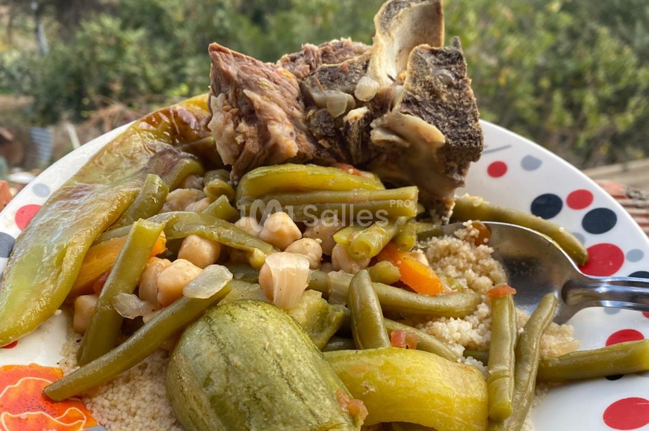 Assiette de couscous avec légumes variés, pois chiches et morceaux de viande, servie en extérieur.