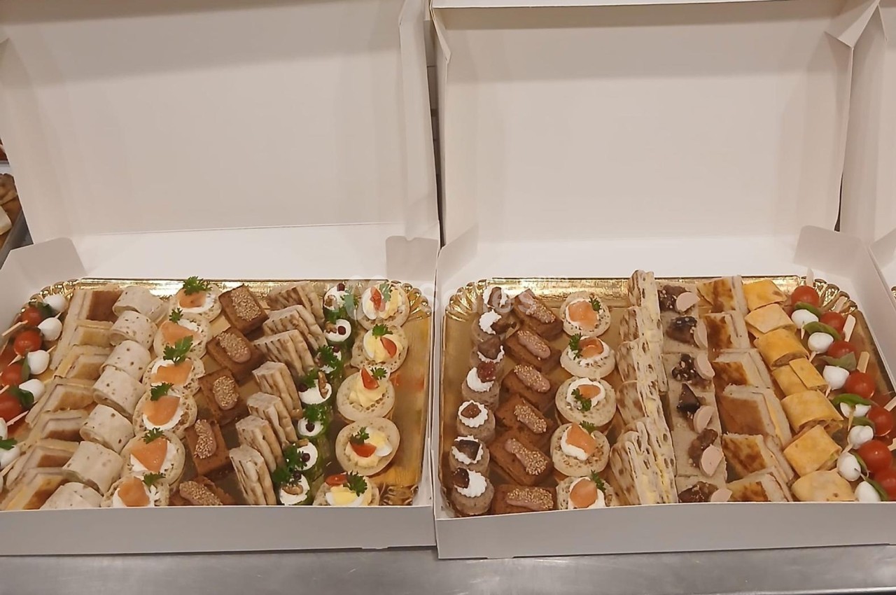 Plateaux garnis de divers amuse-bouches, incluant toasts, roulés, œufs mimosa et bouchées salées, présentés dans des boîtes…