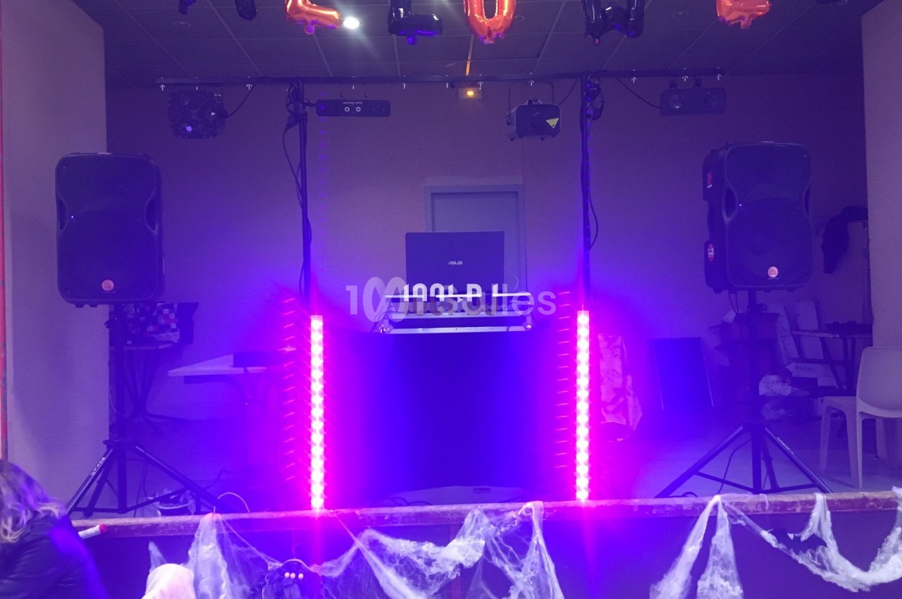 Poste de DJ éclairé par des lumières violettes, entouré de décorations d'Halloween et de toiles d'araignée.