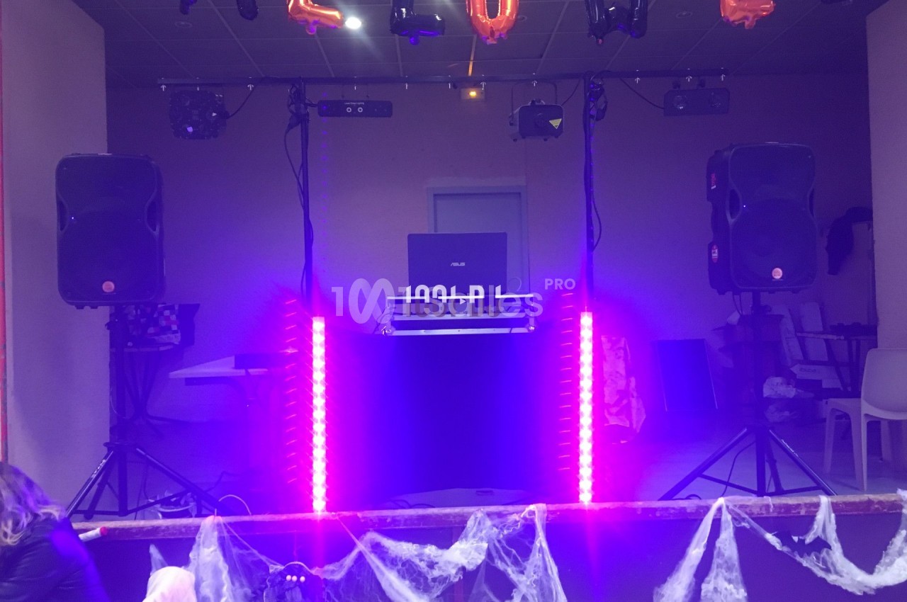 Poste de DJ éclairé par des lumières violettes, entouré de décorations d'Halloween et de toiles d'araignée.