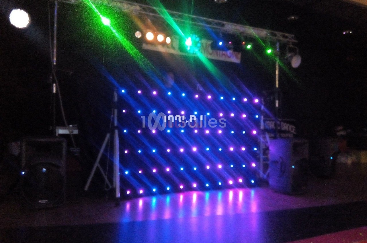 Pupitre de DJ illuminé par des lumières LED colorées, entouré d'équipements audio dans une salle sombre.