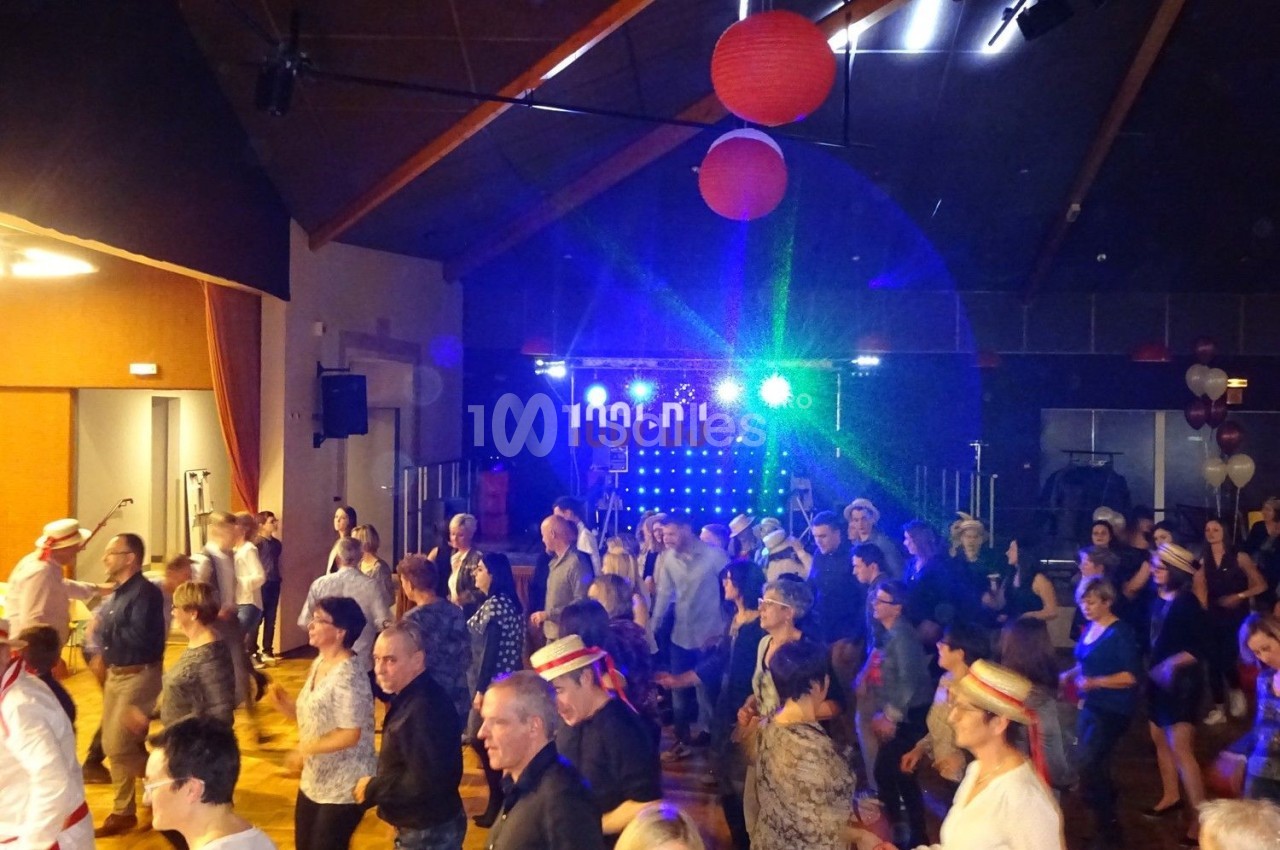 Groupe de personnes dansant dans une salle éclairée par des lumières colorées, avec une scène en arrière-plan.