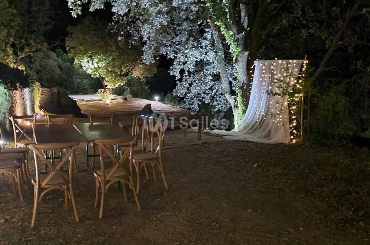 Espace extérieur nocturne avec table et chaises en bois, éclairage doux et décor lumineux sous des arbres.