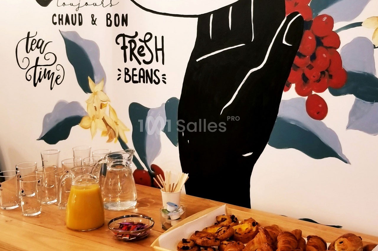 Table en bois avec viennoiseries, jus d'orange, verres et carafe devant une fresque murale colorée sur le café.