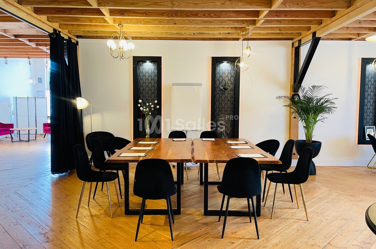 Salle de réunion lumineuse avec une grande table en bois entourée de chaises noires, éclairée par des suspensions.