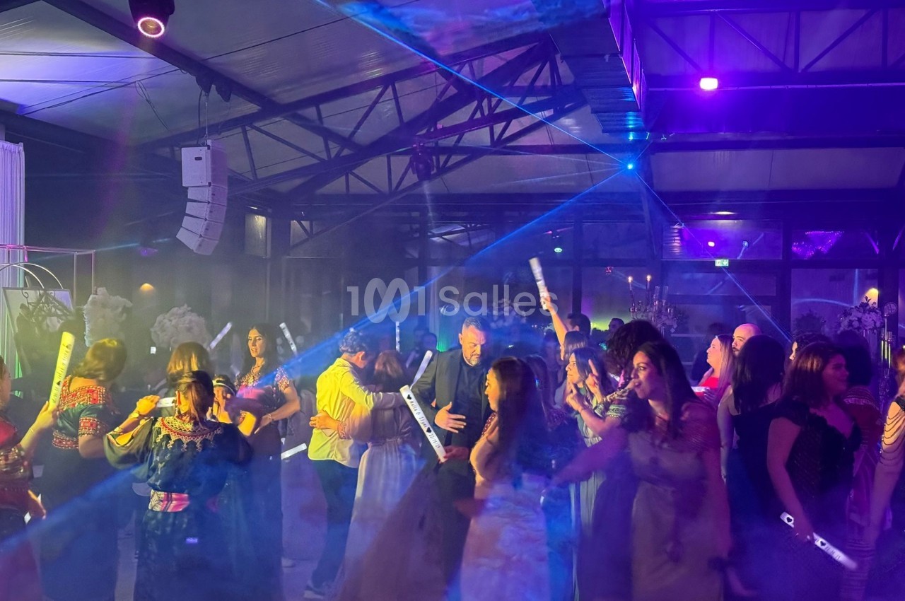 Des personnes dansent sous des lumières colorées et des faisceaux laser dans une salle de fête animée.