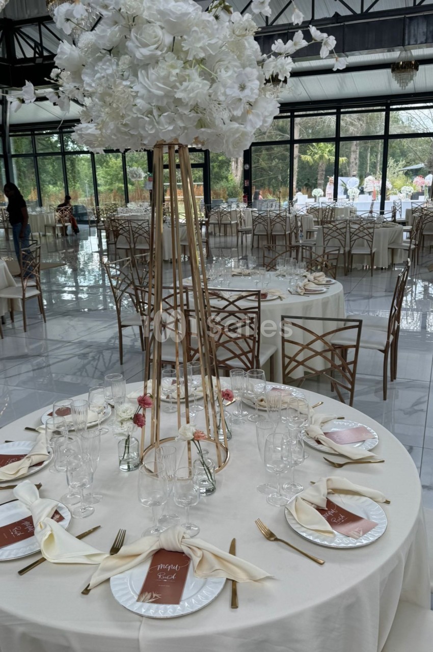 Table de réception élégamment dressée avec nappes blanches, couverts dorés et centre de table floral blanc.
