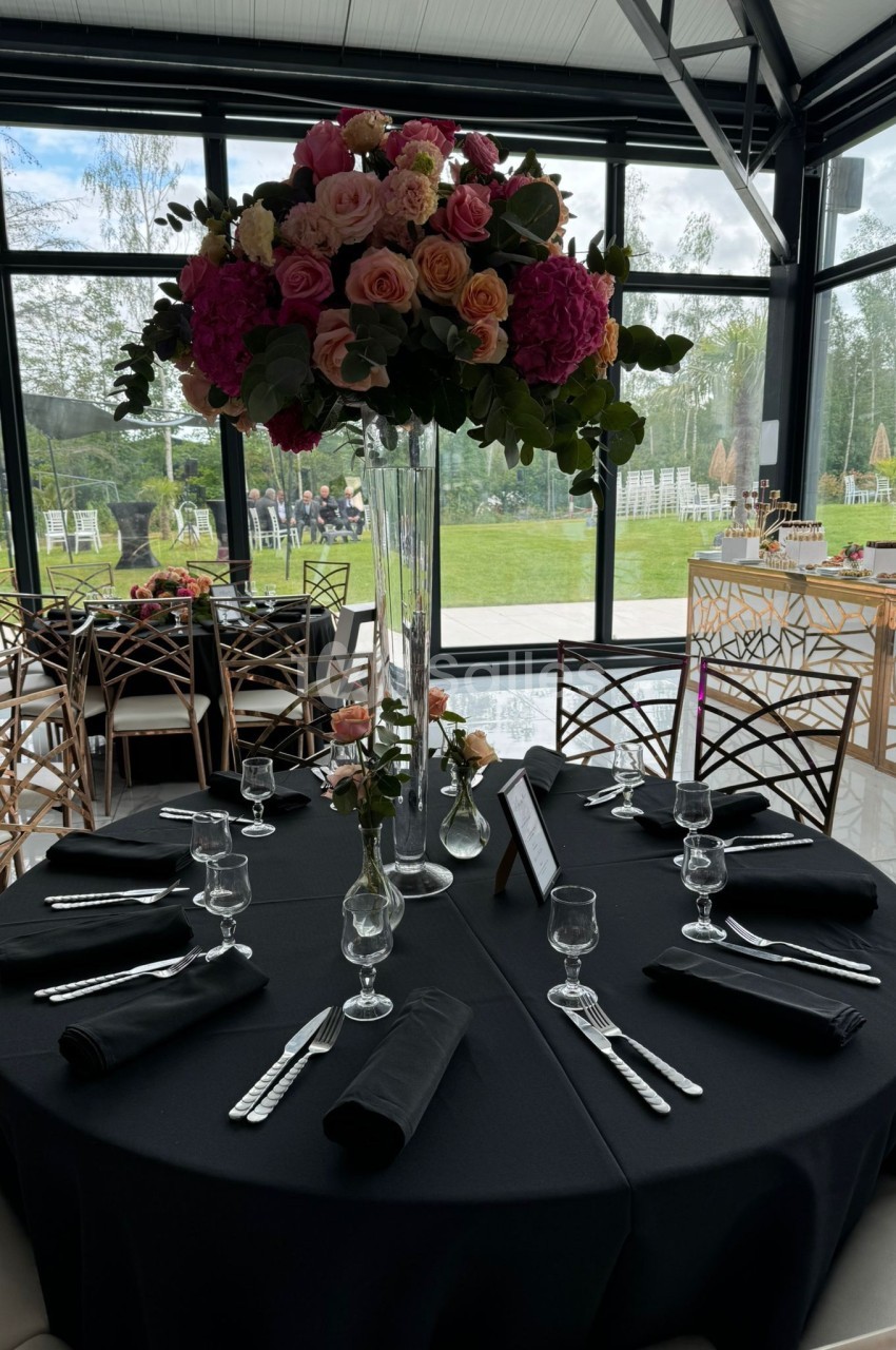 Table dressée avec une nappe noire, couverts disposés, et un grand bouquet de fleurs colorées en centre de table.