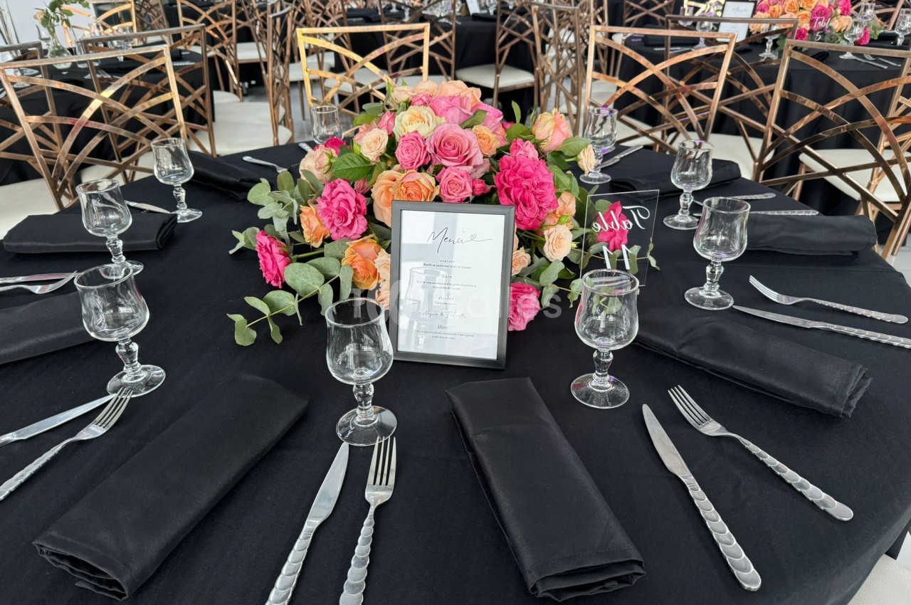 Table dressée avec une nappe noire, couverts argentés, verres, serviettes noires et un centre de table floral coloré.