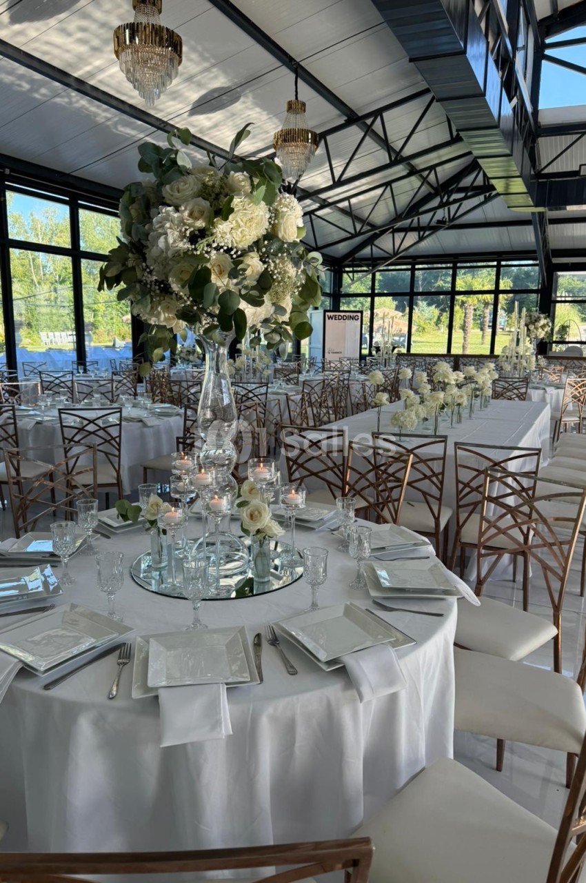 Salle de réception lumineuse avec tables décorées de fleurs blanches, chandeliers et vaisselle élégante.