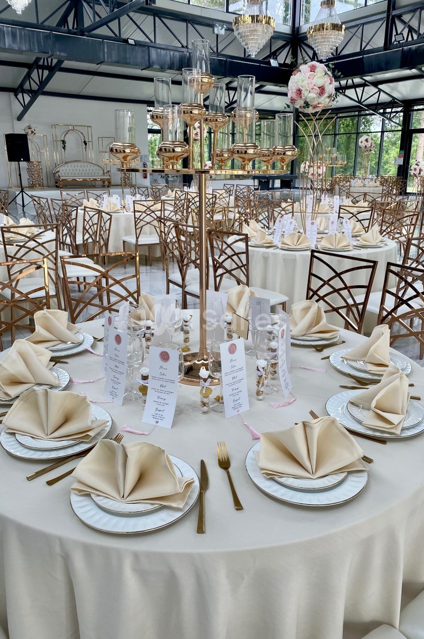 Table élégamment dressée avec nappes blanches, serviettes pliées, vaisselle raffinée et décorations dorées dans une salle…