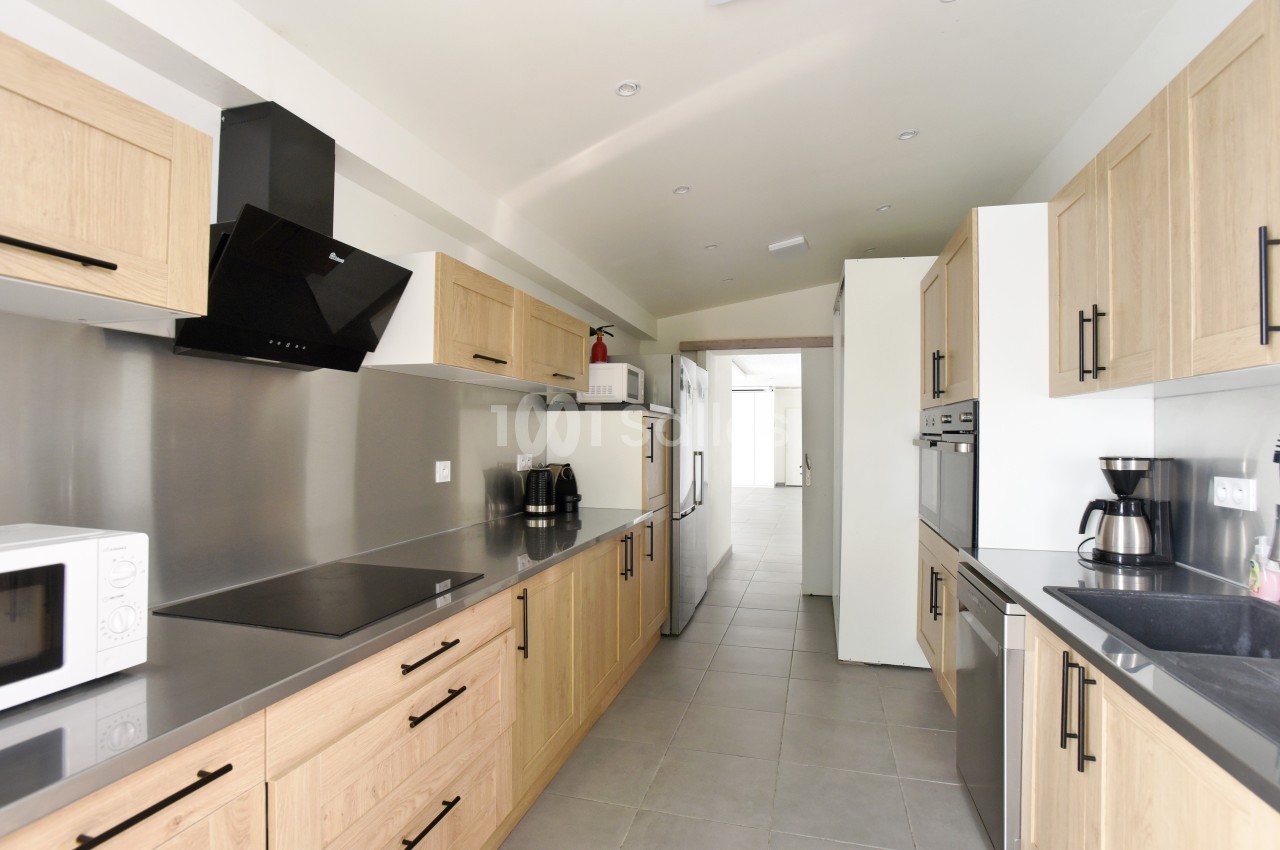 Cuisine moderne avec meubles en bois clair, plan de travail gris, électroménagers intégrés et sol en carrelage gris.