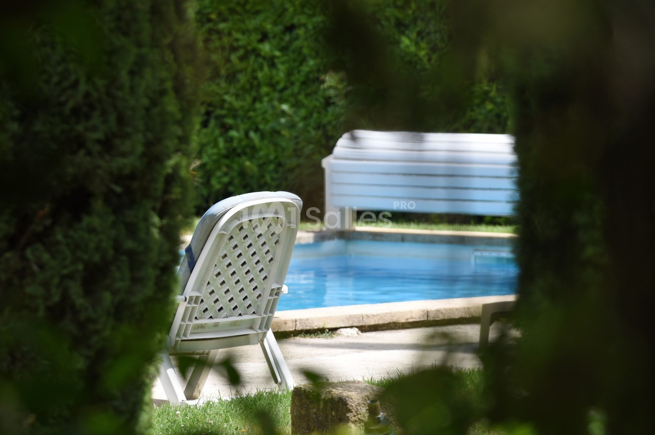 Chaise blanche et banc près d'une piscine entourée de végétation dense.