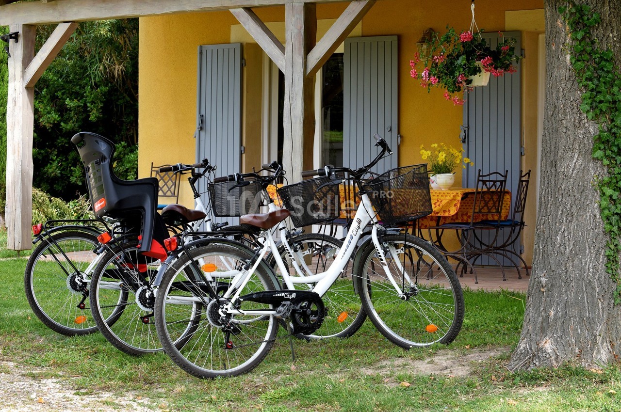Trois vélos stationnés devant une maison avec des volets bleus, une terrasse et une table de jardin.