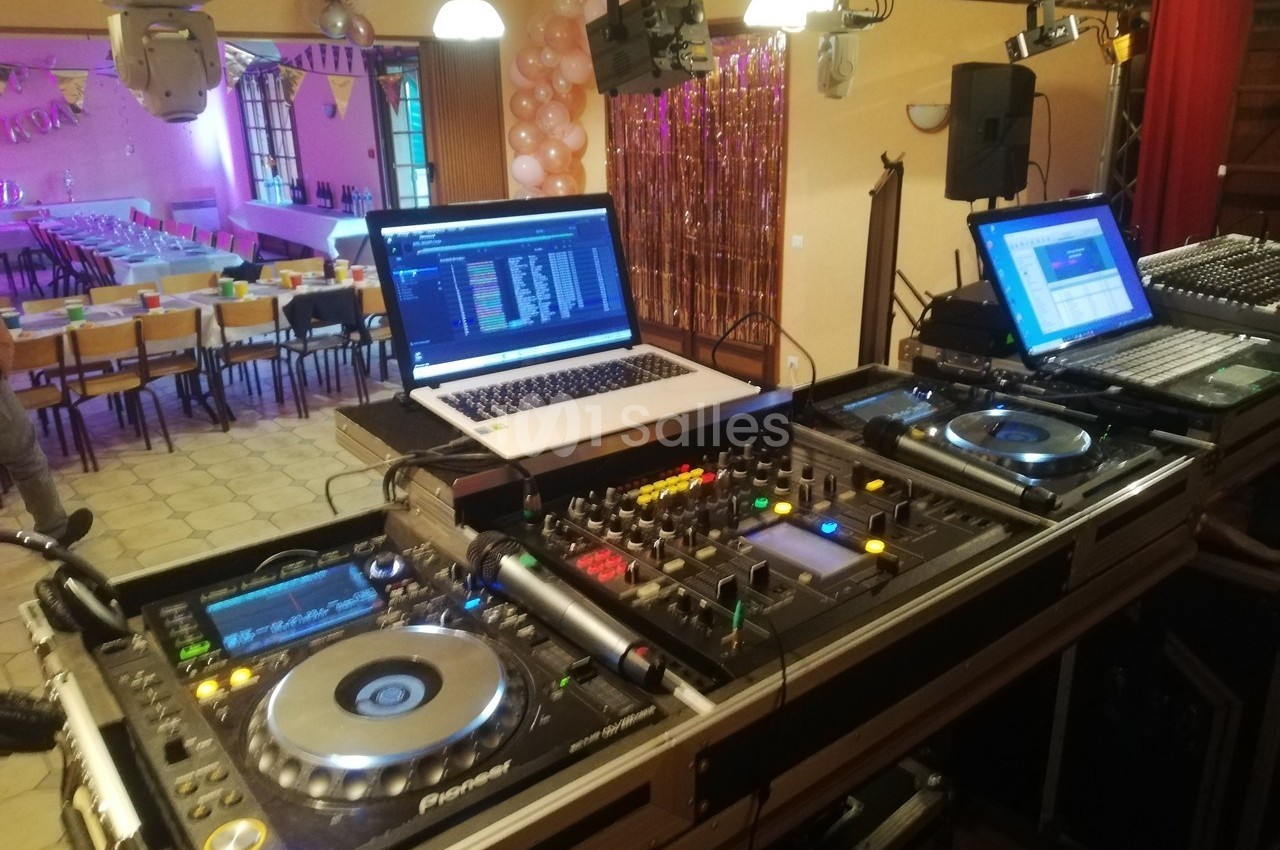 Équipement de DJ avec platines, table de mixage et ordinateurs dans une salle décorée pour un événement festif.