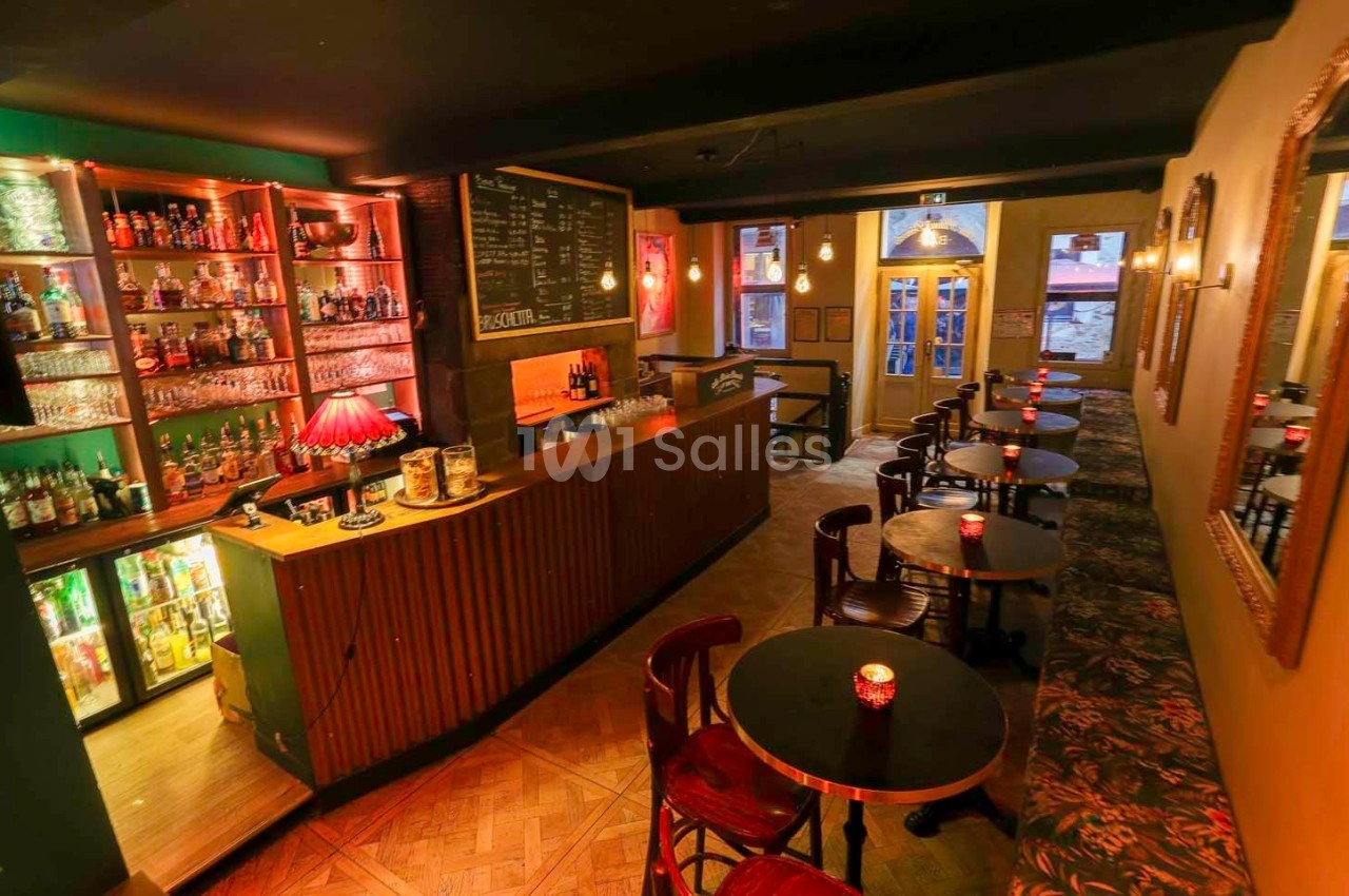 Intérieur d'un bar chaleureux avec comptoir en bois, étagères de bouteilles et petites tables éclairées par des bougies.