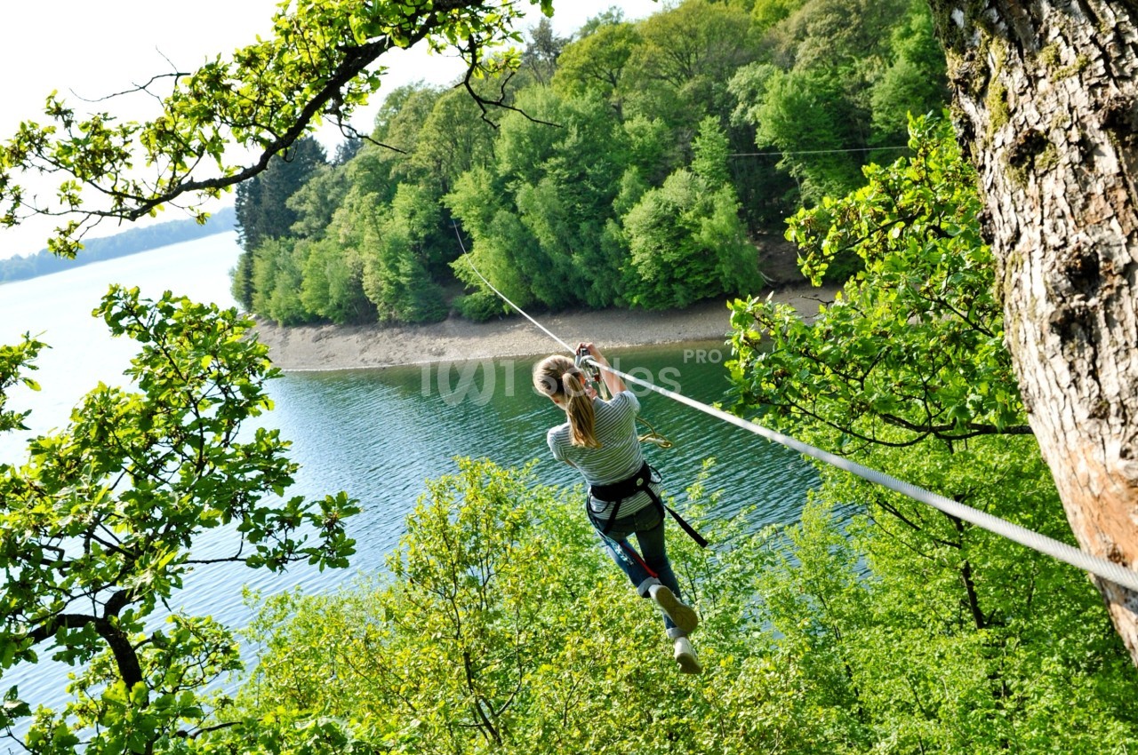Une personne traverse un lac sur une tyrolienne entourée de forêt verdoyante.