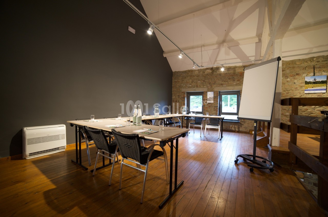 Salle de réunion lumineuse avec tables, chaises, paperboard et bouteilles d'eau sur un sol en bois.