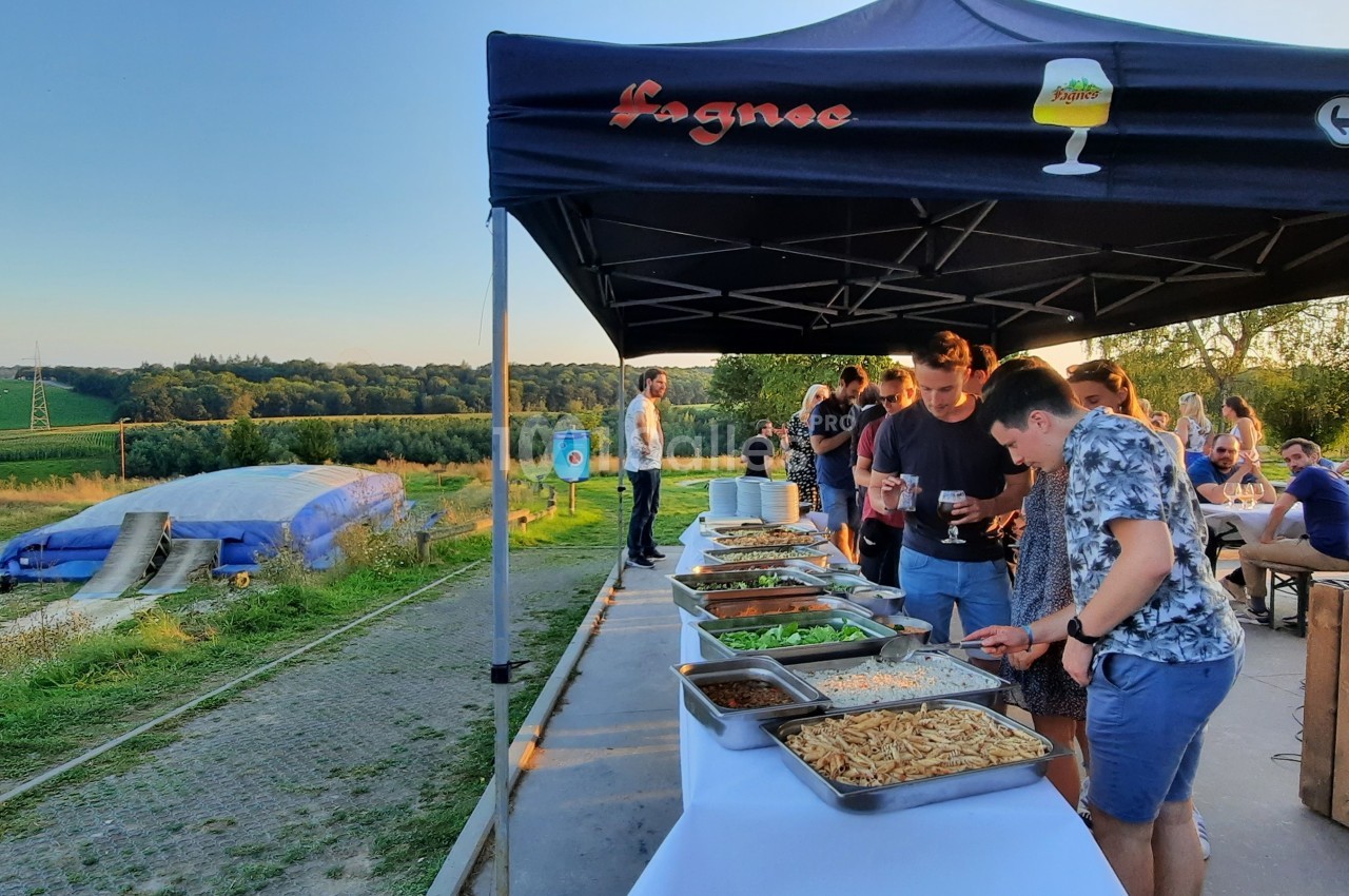 Des personnes se servent à un buffet en plein air sous une tente, avec un paysage champêtre en arrière-plan.