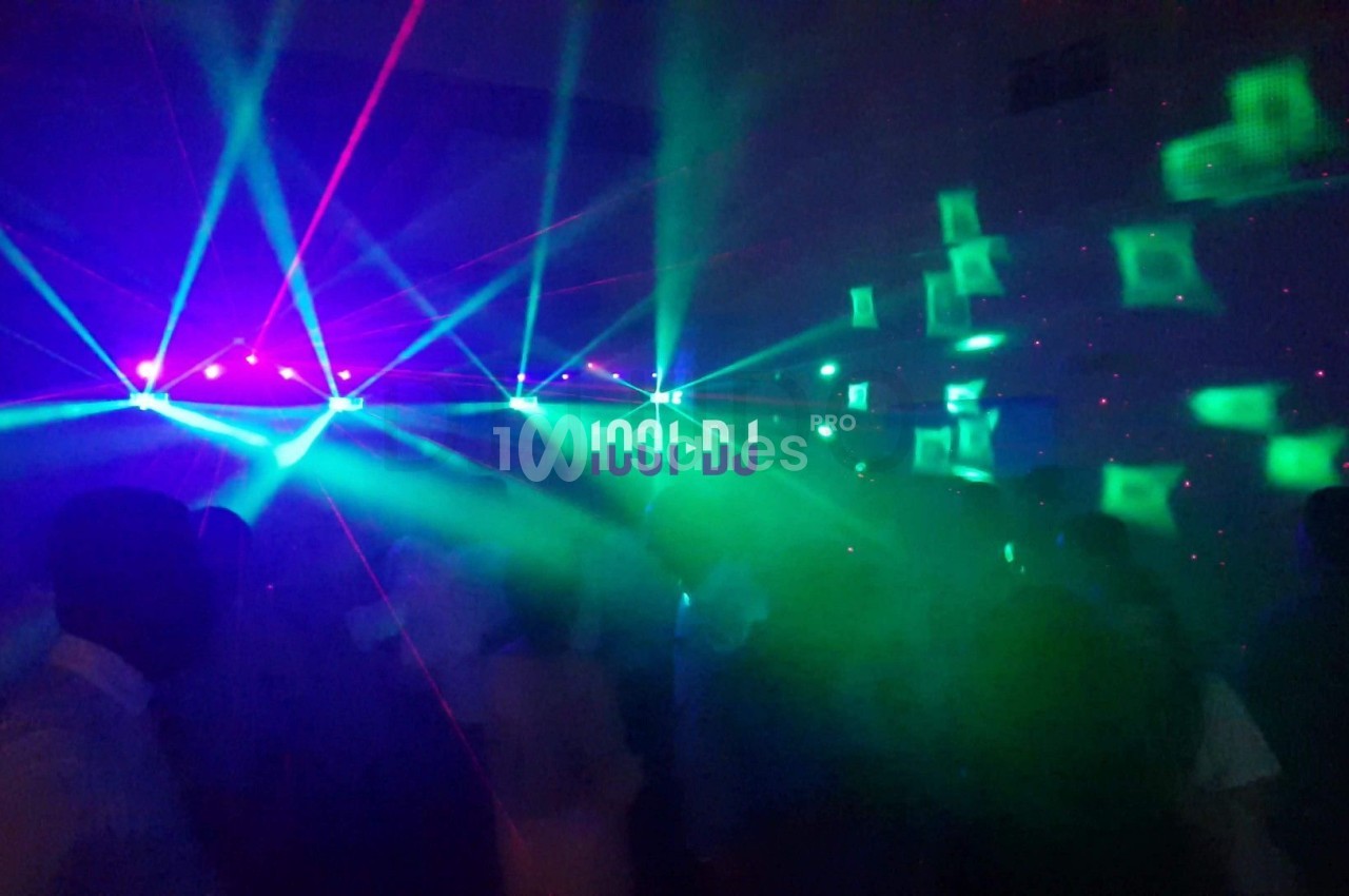 Salle sombre avec des jeux de lumières colorées, des lasers et une foule dans une ambiance festive.
