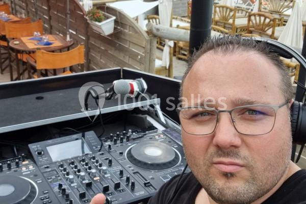 Un homme portant un casque audio devant une table de mixage, en extérieur près d'une terrasse aménagée.
