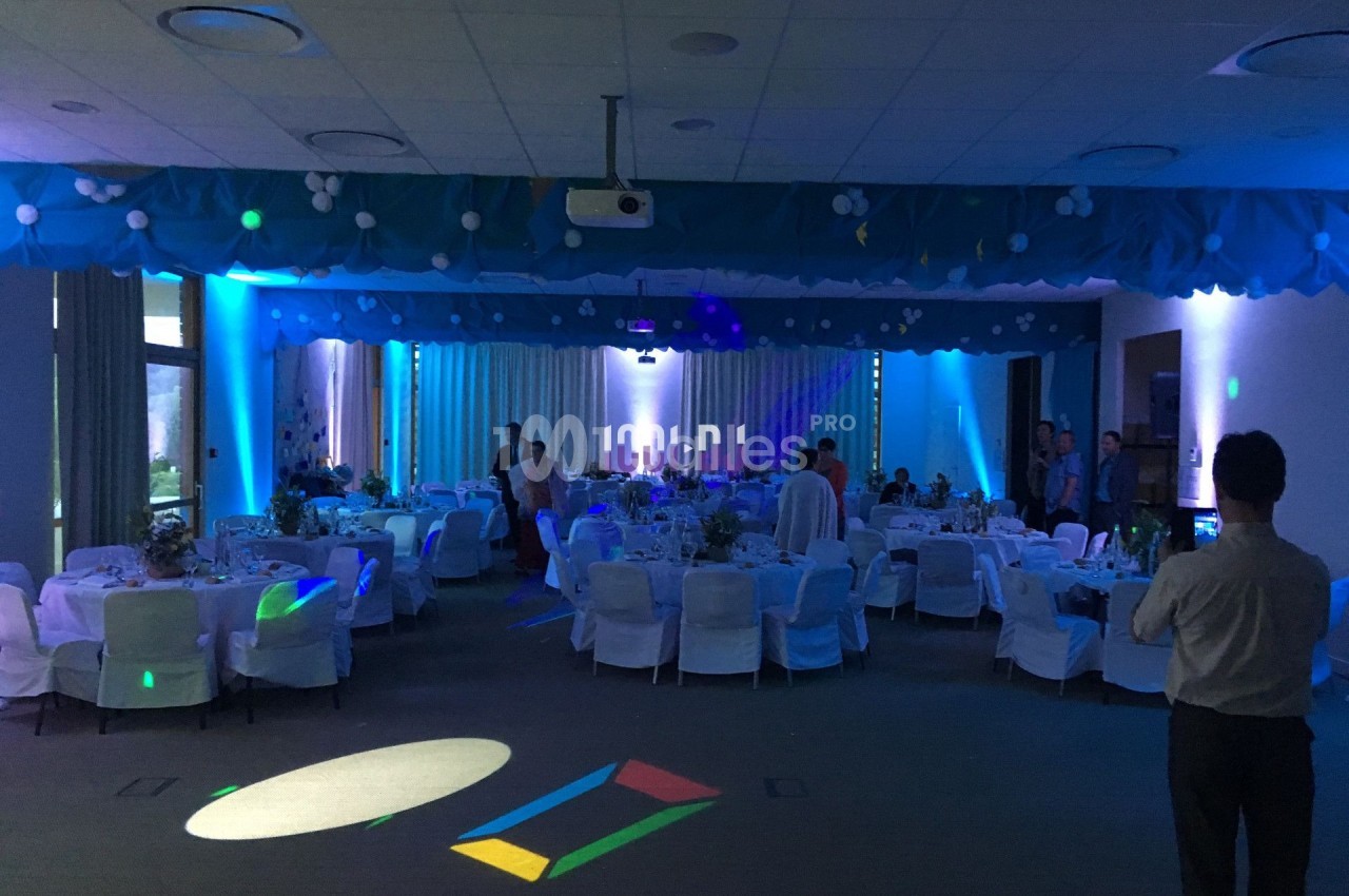 Salle de réception décorée avec des tables rondes, nappes blanches et éclairage tamisé bleu.