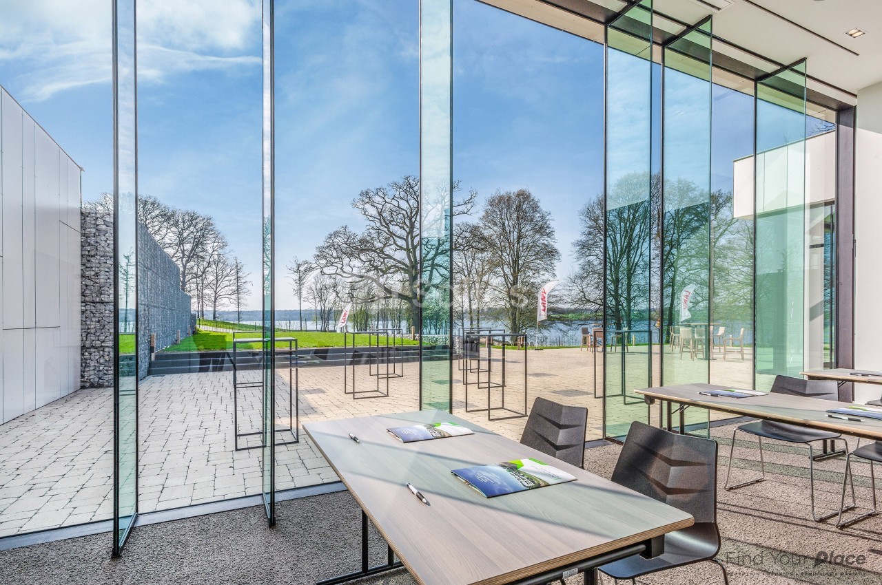 Salle lumineuse avec de grandes baies vitrées donnant sur un espace extérieur arboré et aménagé.