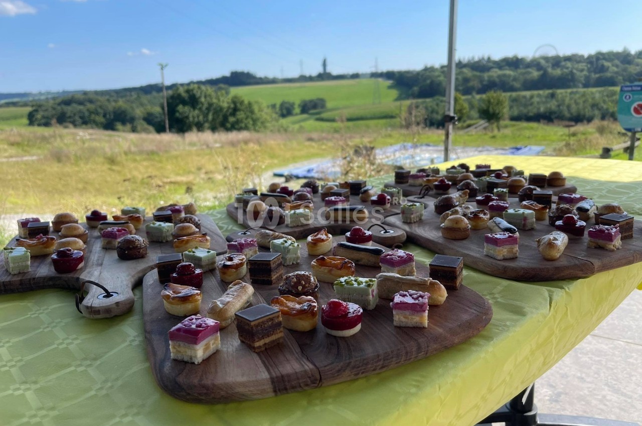 Plateaux de mignardises variées disposés sur une nappe jaune en extérieur avec vue sur un paysage champêtre.