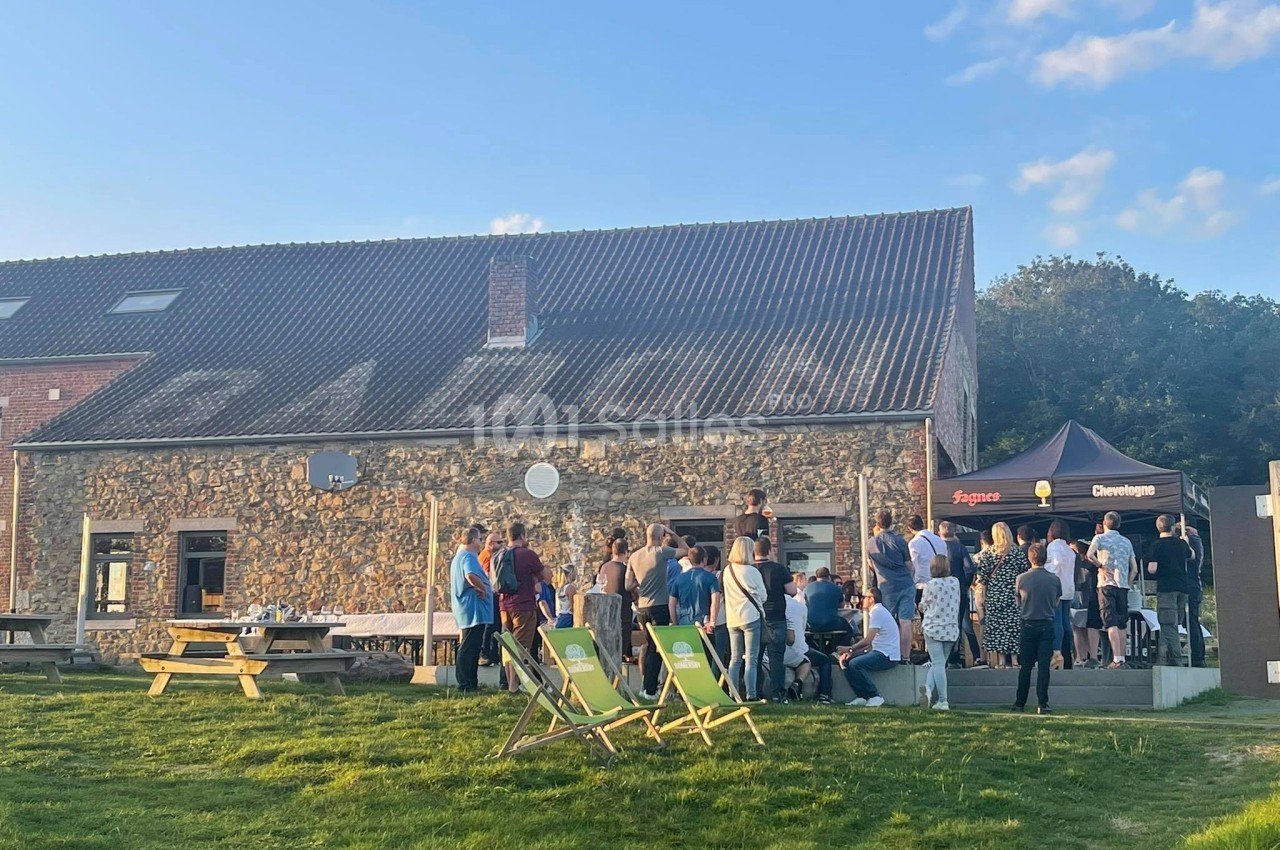 Groupe de personnes rassemblées devant un bâtiment en pierre avec des chaises longues sur une pelouse.