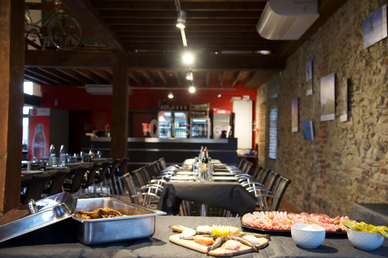 Salle de restaurant avec tables dressées, plats de charcuterie et buffet en premier plan, murs en pierre apparente.