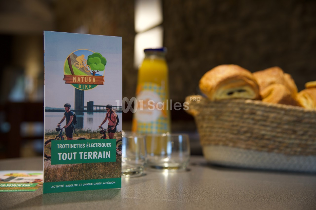 Dépliant sur des trottinettes électriques tout terrain posé sur une table avec viennoiseries et jus d'orange en arrière-plan.