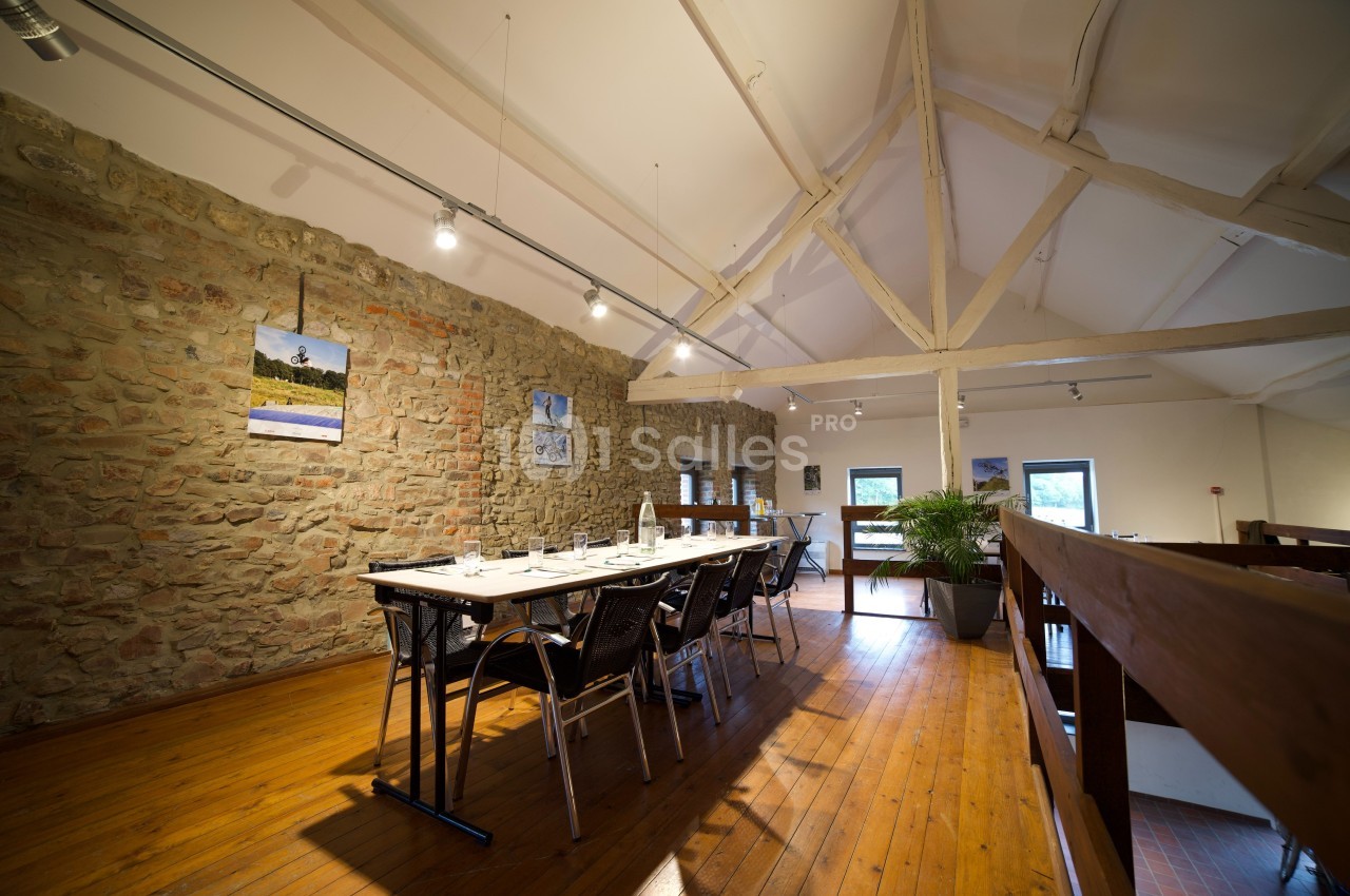 Salle à manger lumineuse avec table dressée, murs en pierre apparente, poutres blanches et parquet en bois.