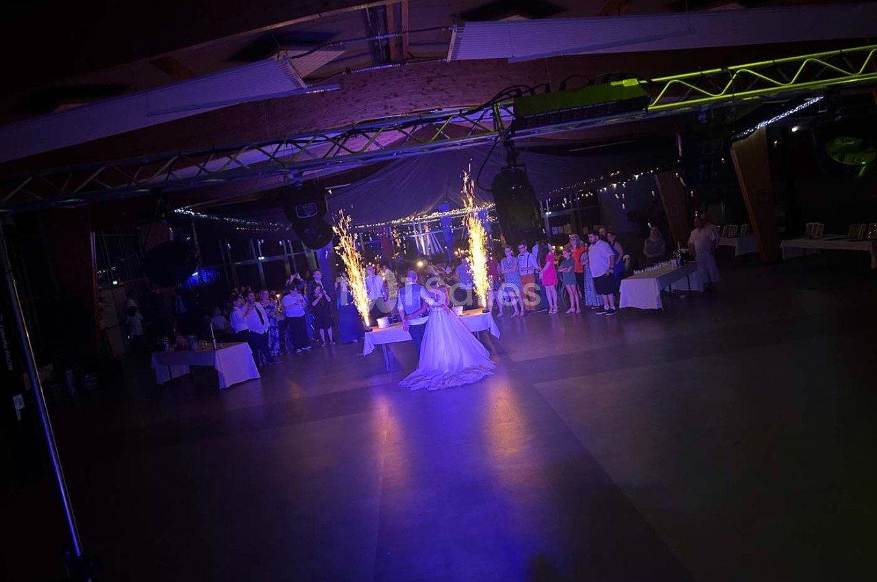 Un couple danse au centre d'une salle éclairée, entouré d'invités et de jets de lumière scintillants.