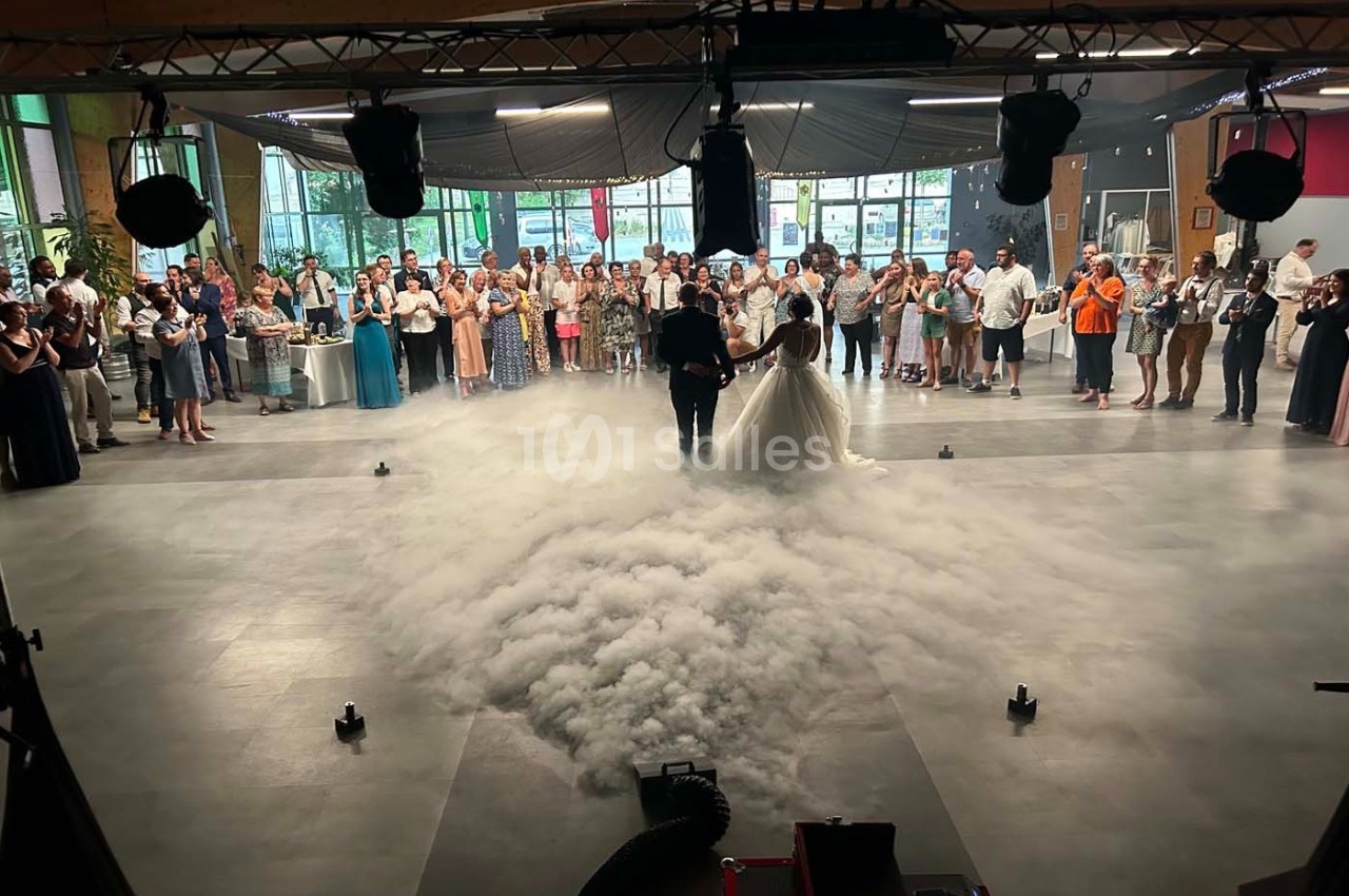 Un couple danse au centre d'une salle décorée, entouré de fumée au sol et d'invités observant la scène.