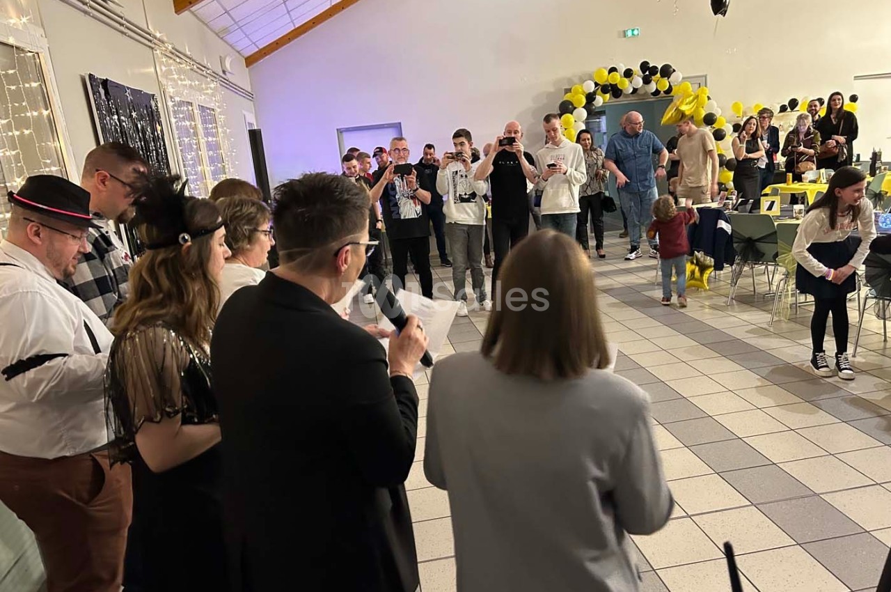 Groupe de personnes rassemblées dans une salle décorée de ballons noirs et jaunes, lors d'un événement festif.