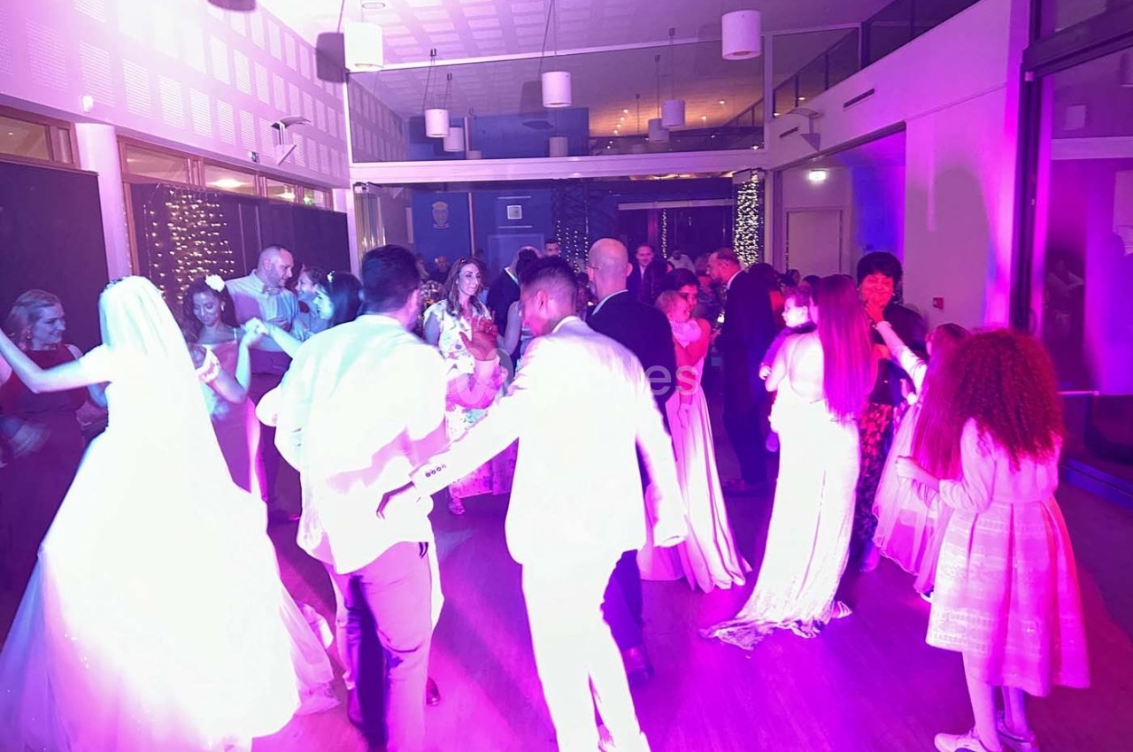 Des invités dansent dans une salle éclairée de lumières colorées, lors d'une fête ou d'une célébration.